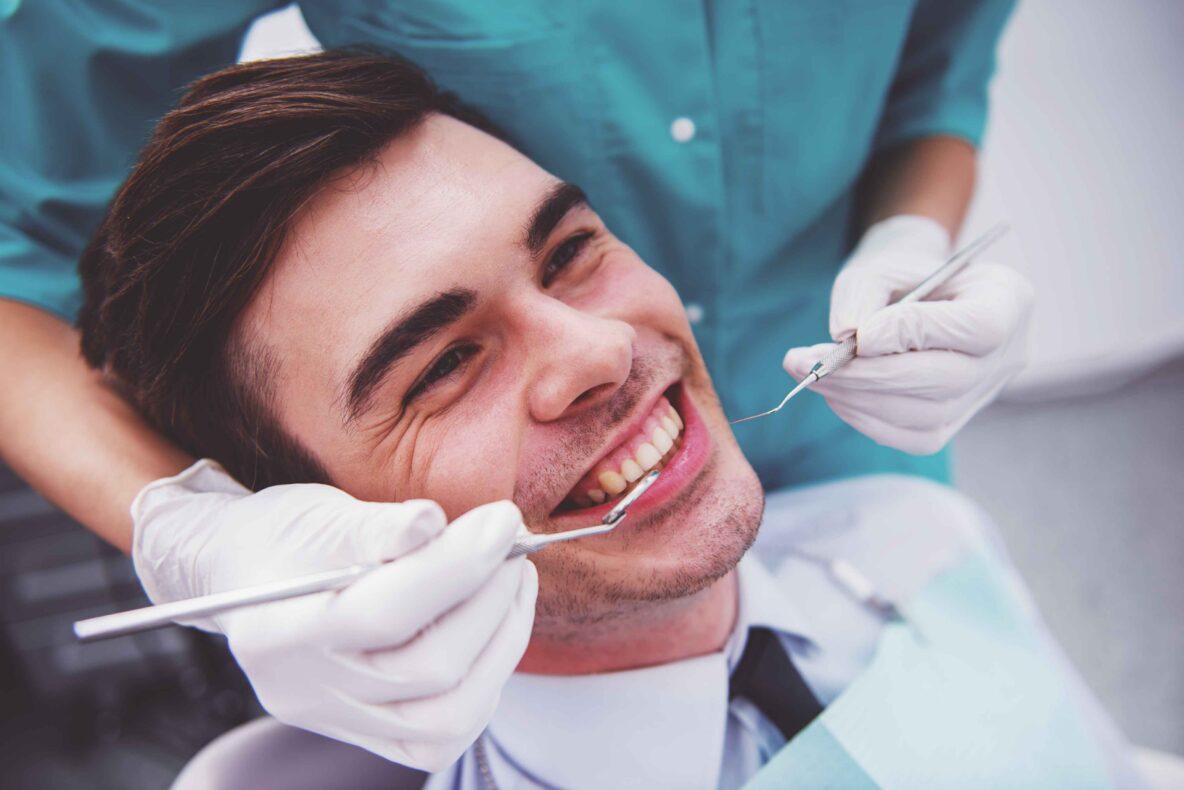 Patient smiling during a dental exam while a dentist checks their teeth.