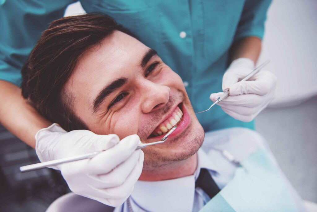 Patient smiling during a dental exam while a dentist checks their teeth.