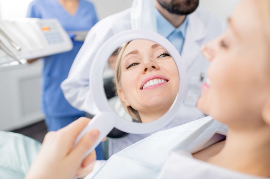 Patient smiling and checking teeth in a dental mirror.
